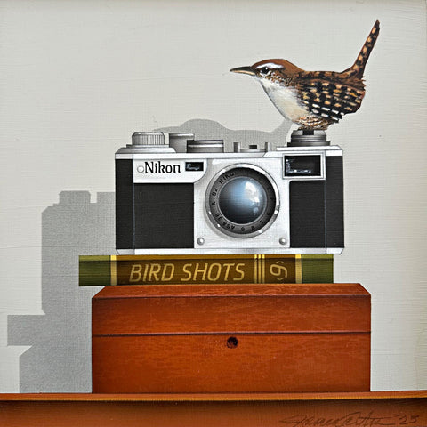 Trompe-l'œil painting of a winter wren sitting on a Nikon camera atop a book titled "Bird Shots" and a wooden box against a white background by James Carter - Cottage Curator - Sperryville VA Art Gallery
