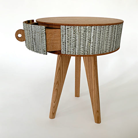 View of small round three-legged end table with open drawer and horizontal striping around the sides made of ash, cork and milkpaint by Christina Boy at Cottage Curator - Sperryville VA Art Gallery