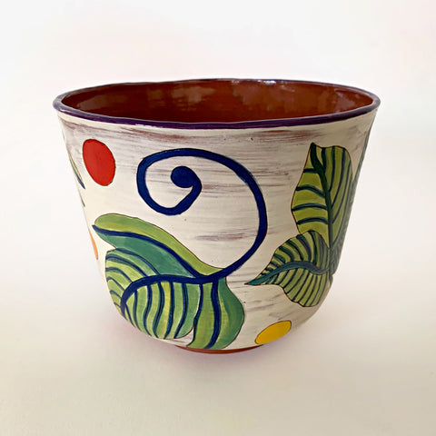 Ceramic vessel with clay red interior and white exterior decorated with bold green and blue plant leaves, with red and yellow dots surrounding, by artist Sara Schneidman at Cottage Curator - Sperryville VA Art Gallery