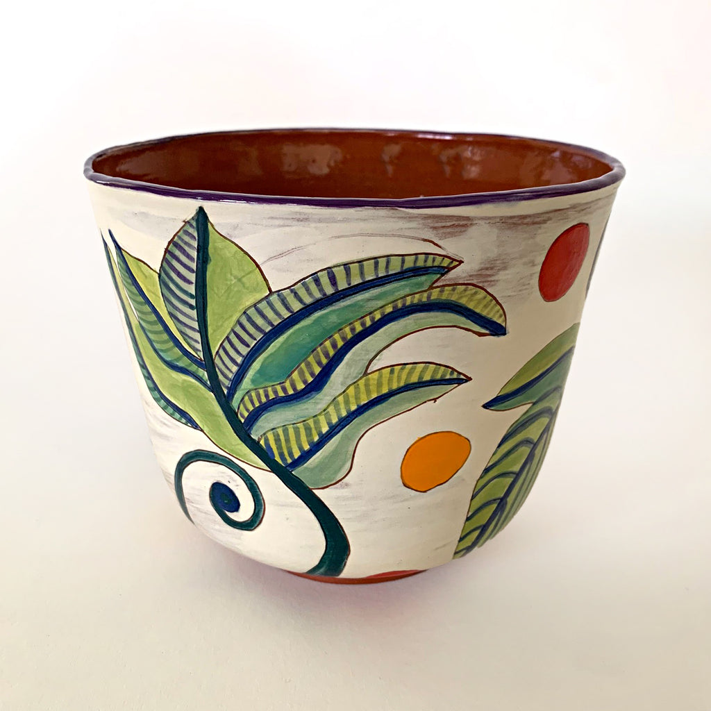 Ceramic vessel with clay red interior and white exterior decorated with bold green and blue plant leaves, with red and yellow dots surrounding, by artist Sara Schneidman at Cottage Curator - Sperryville VA Art Gallery